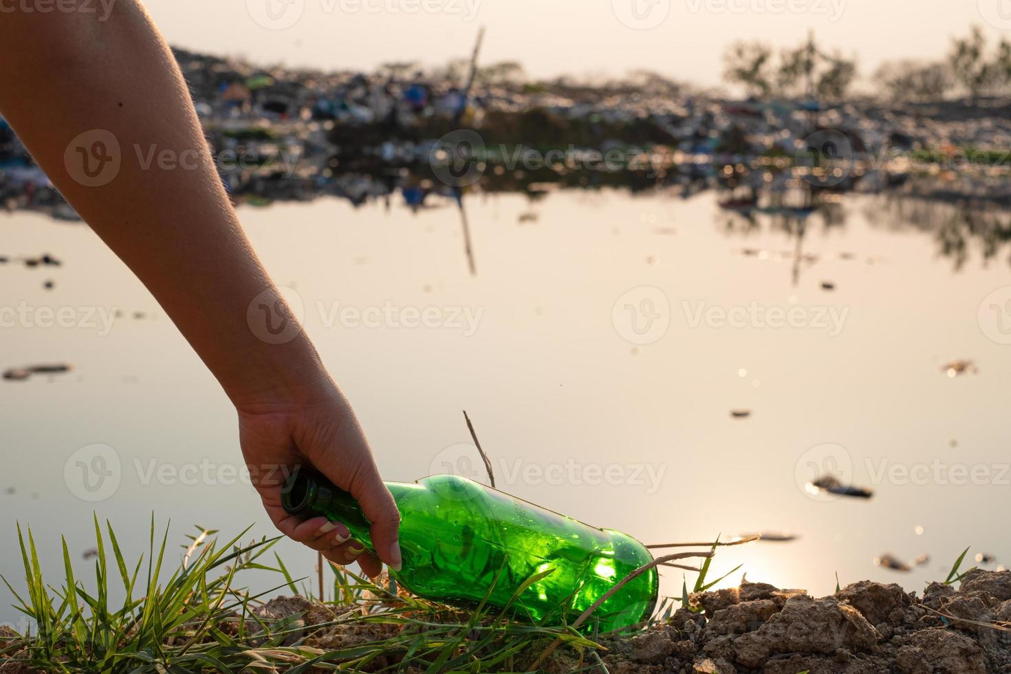 Handaufheben grüne Glasflasche und Flasche am großen Müllhintergrund des Berges foto