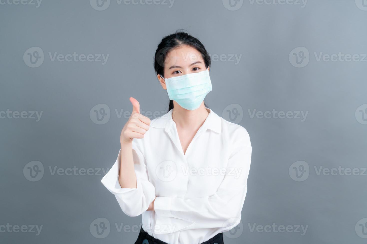 junge asiatische frau, die medizinische gesichtsmaske trägt und daumen hochgibt foto