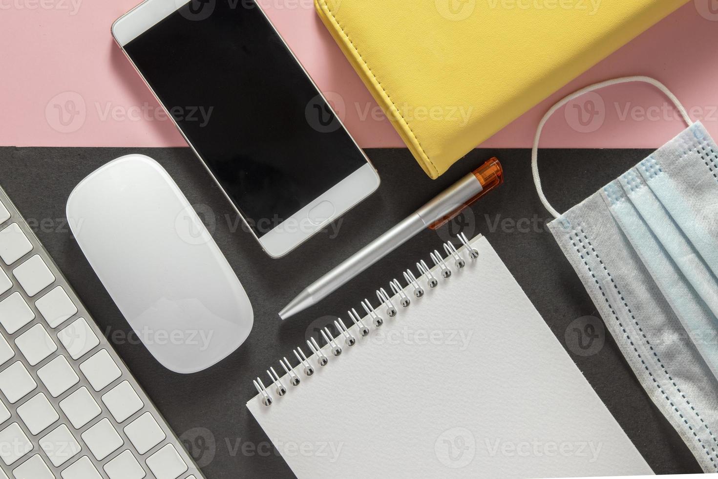 flacher Lay-Desktop mit Tastatur, Telefon, medizinischer Maske, Notizblock auf farbigem Hintergrund foto