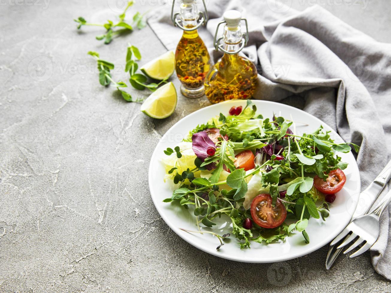 frische grüne gemischte salatschüssel mit tomaten und microgreens auf konkretem hintergrund. gesundes Essen, Ansicht von oben. foto