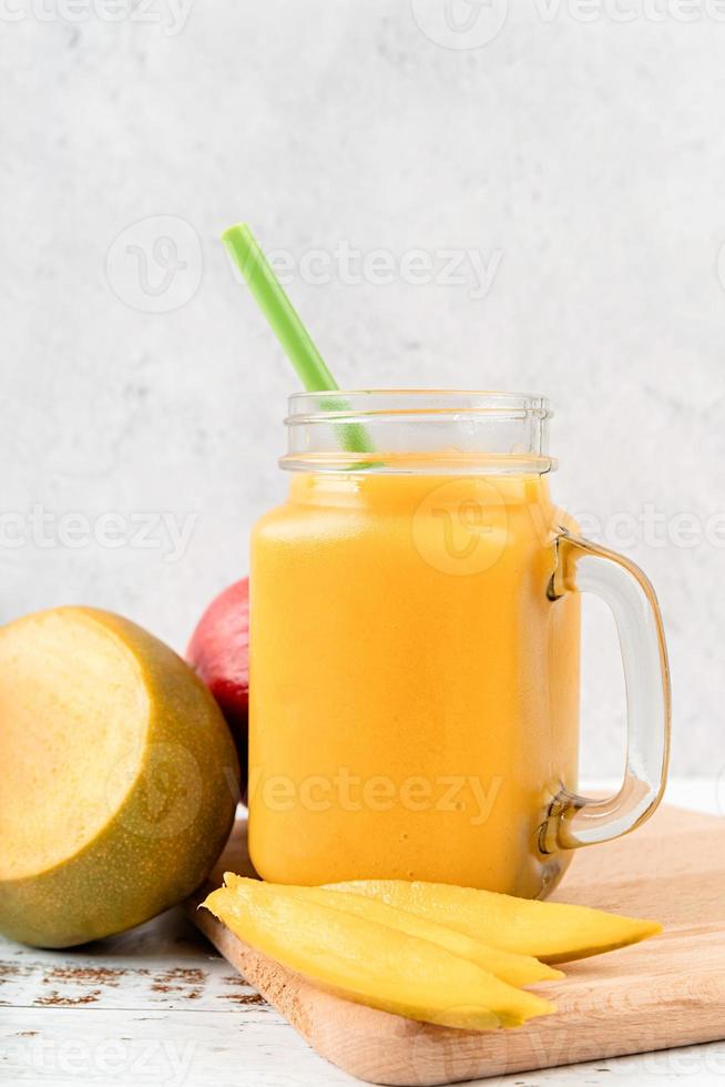 Mango-Smoothie in einem Einmachglas, dekoriert mit Mangoscheiben, Vorderansicht auf Holzhintergrund foto
