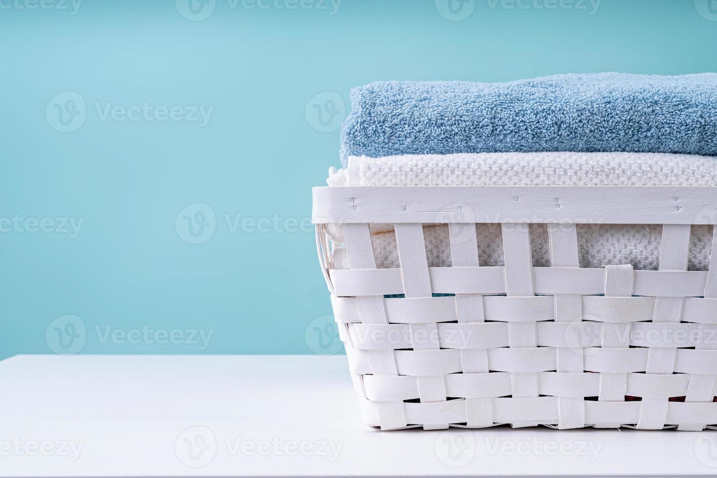 Stapel saubere Handtücher in einem weißen Wäschekorb auf blauem Hintergrund foto