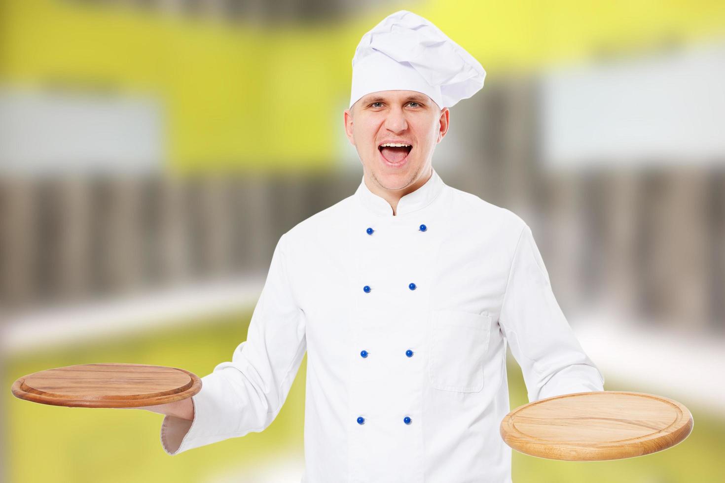 lächelnder Koch mit leeren hölzernen Pizzabrettern in seinem Küchenhaus foto