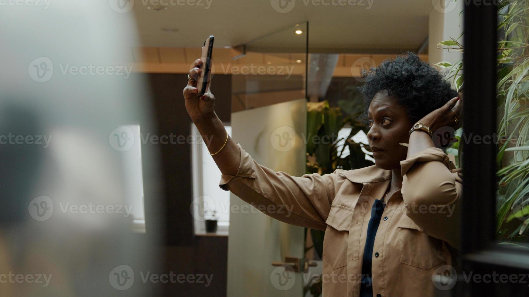 schwarze reife Frau hält Handy in der Luft, stellt ihre Haare ein und schaut auf Telefon foto