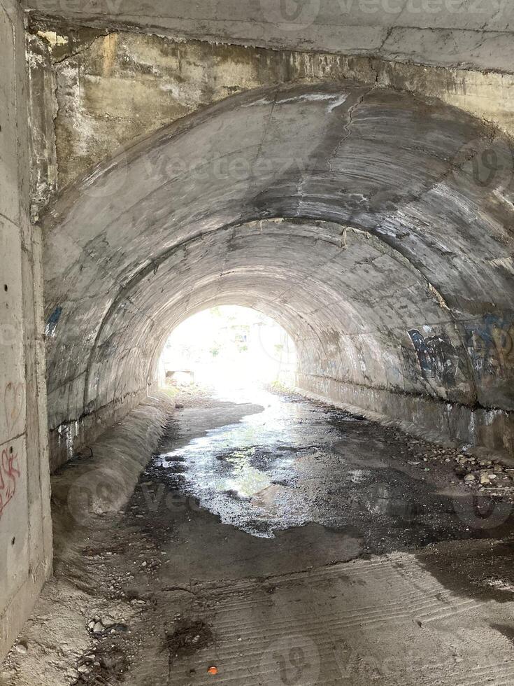 ein alt Tunnel unter das Straße beim das andere Ende Sie können sehen das Sonne foto