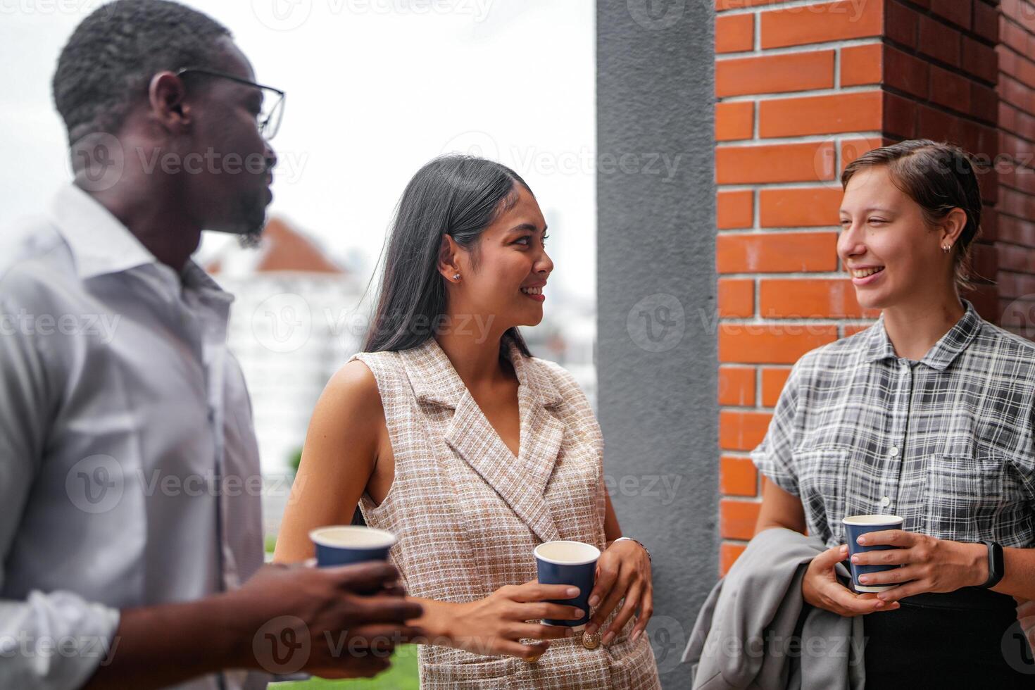 Mannschaft von Geschäft Menschen Clever Mann und Frauen Stand beim draussen Terrasse Gebäude und sich unterhalten zusammen mit Frühstück Essen und Kaffee auf das Hand im gut Gefühl mit Stadt Raum Gebäude. Geschäft Morgen. foto