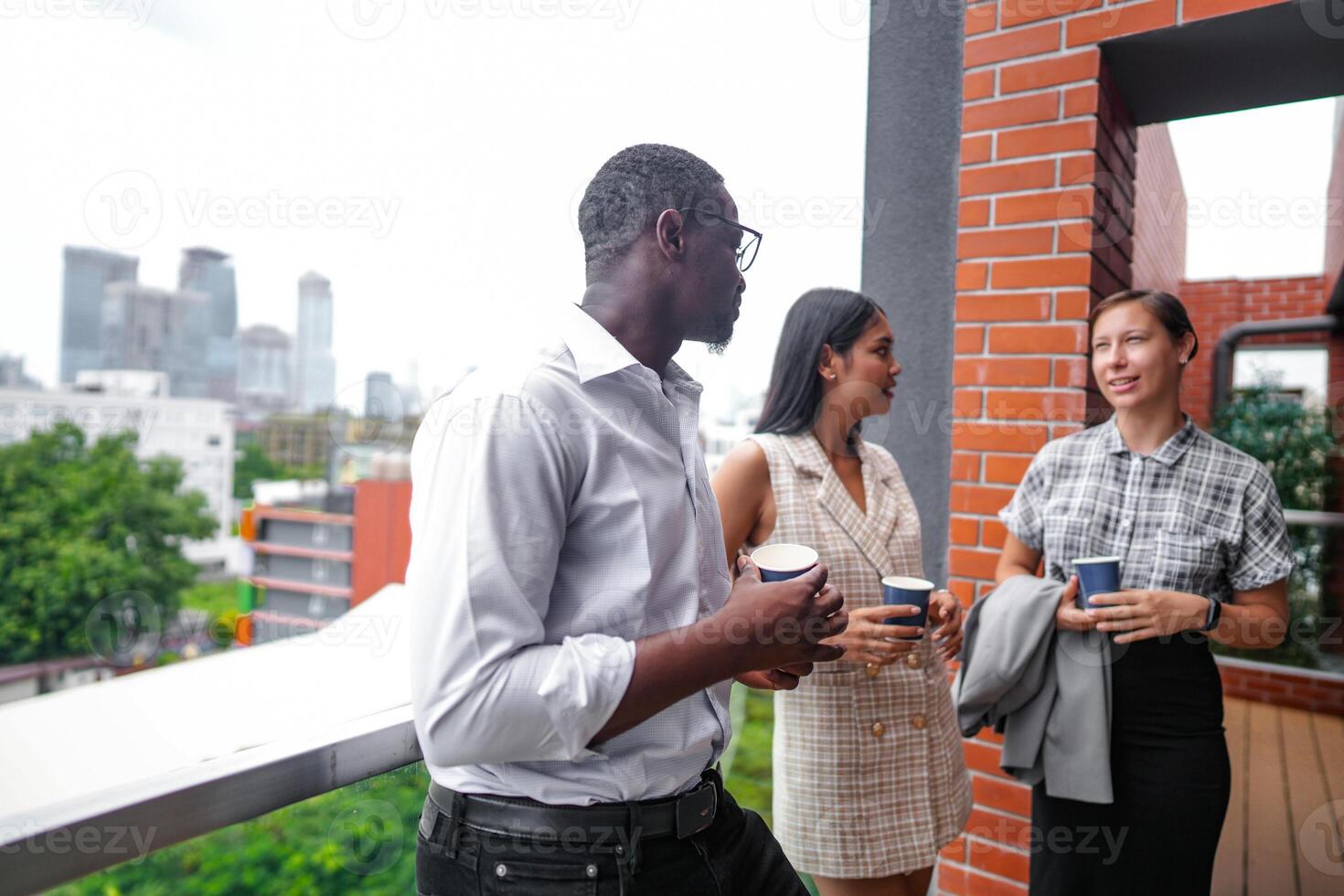 Mannschaft von Geschäft Menschen Clever Mann und Frauen Stand beim draussen Terrasse Gebäude und sich unterhalten zusammen mit Frühstück Essen und Kaffee auf das Hand im gut Gefühl mit Stadt Raum Gebäude. Geschäft Morgen. foto