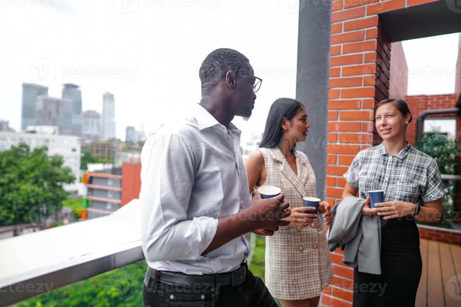 Mannschaft von Geschäft Menschen Clever Mann und Frauen Stand beim draussen Terrasse Gebäude und sich unterhalten zusammen mit Frühstück Essen und Kaffee auf das Hand im gut Gefühl mit Stadt Raum Gebäude. Geschäft Morgen. foto