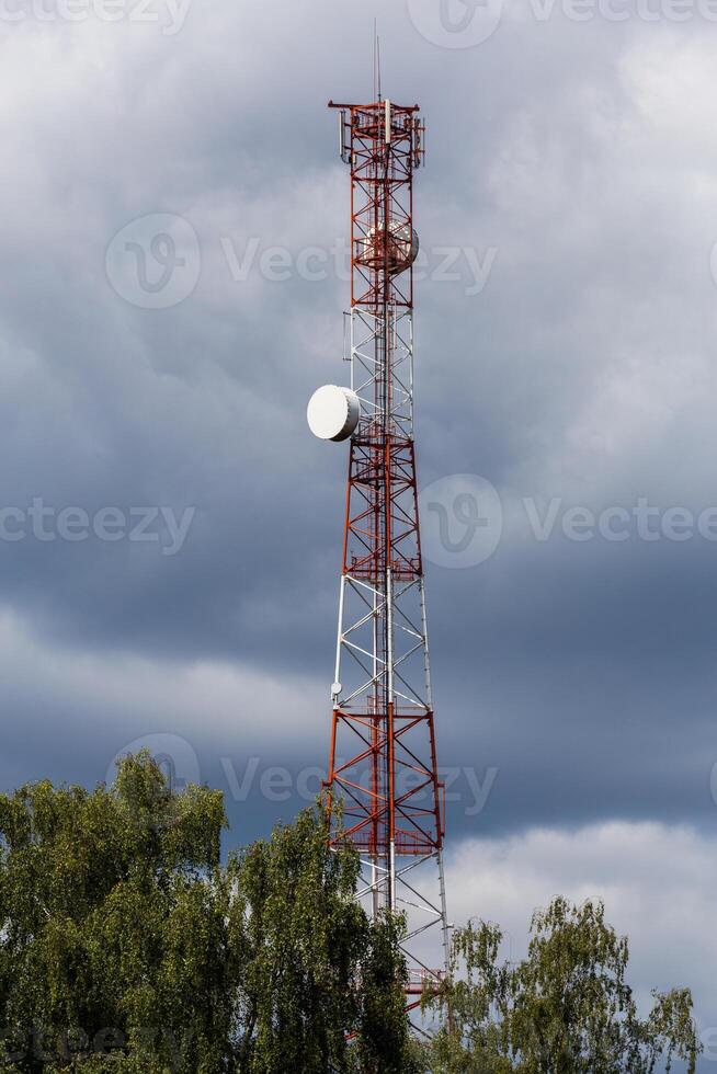 rot-weißer Telekommunikationsturm mit Spitze des grünen Baums auf blauem Himmel mit Wolkenhintergrund foto