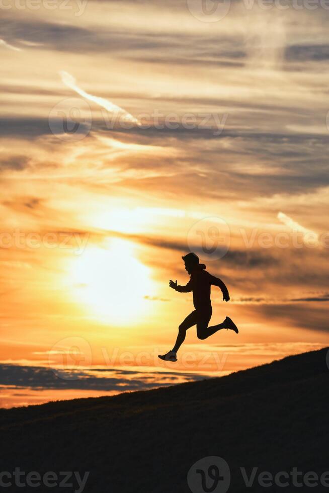 sportlich Mann läuft Nieder Hügel im Silhouette foto
