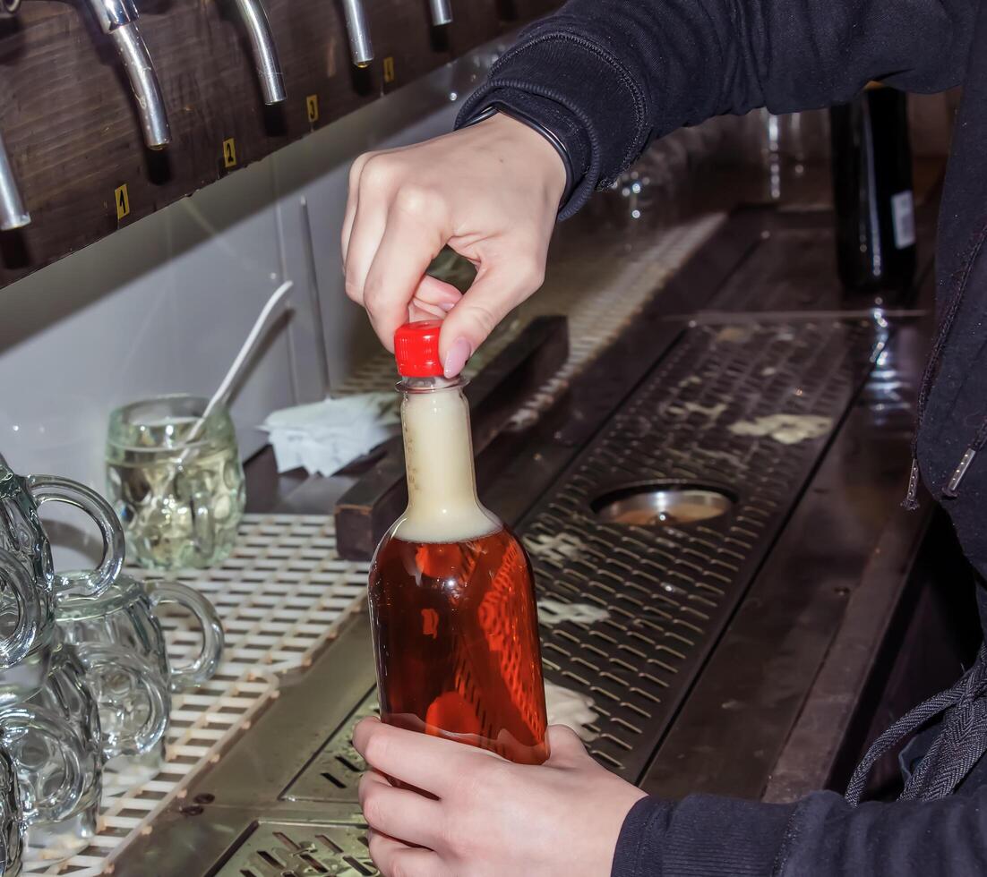 hinter das Schalter. Damen Hände schön und leicht gießen Bier in ein Flasche. foto