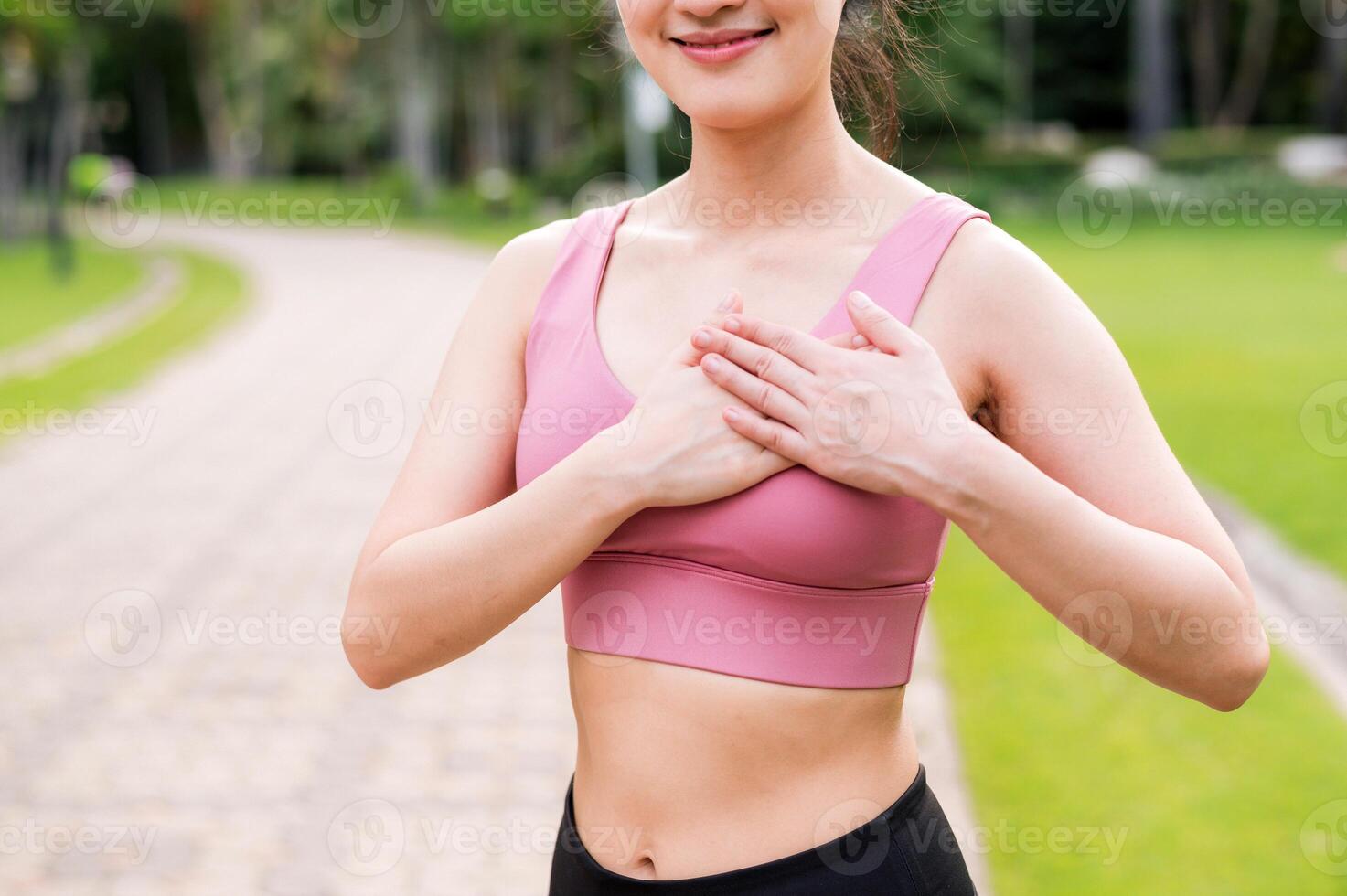 Frau Jogger. jung asiatisch weiblich glücklich Lächeln tragen Rosa Sportbekleidung halten Hände auf Truhe Vor Laufen im Öffentlichkeit Park. Gesundheitswesen Wellness Konzept. foto