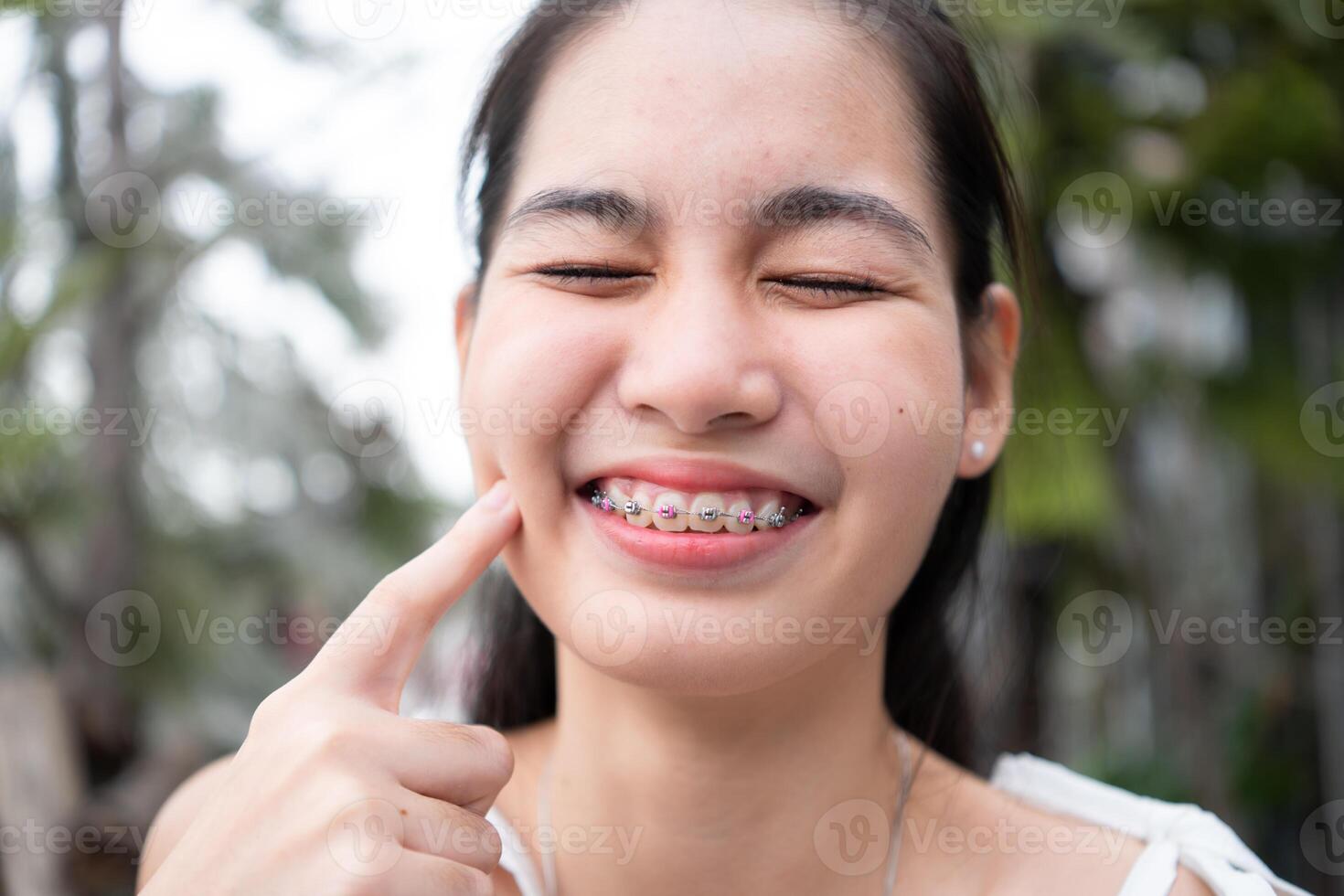 Porträt von ein jung asiatisch Frau mit Hosenträger auf ihr Zähne foto