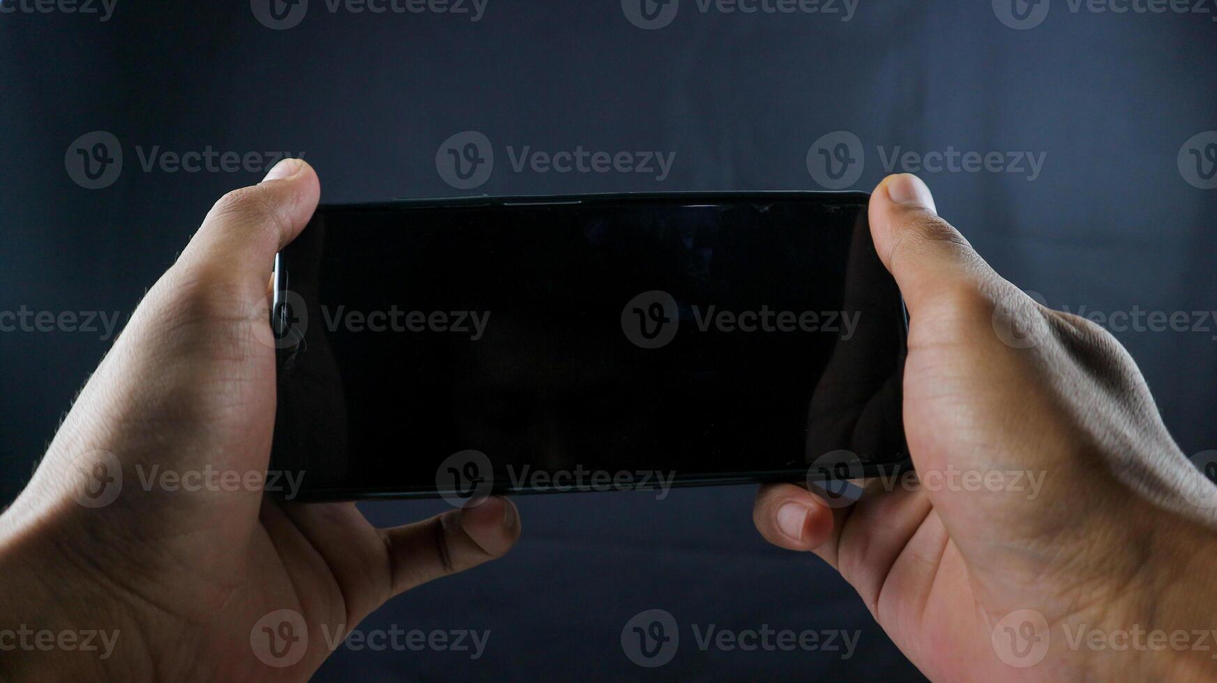 Hand halten Zelle Telefon aussehen mögen spielen ein Spiel leer auf schwarz Bildschirm und schwarz Hintergrund foto