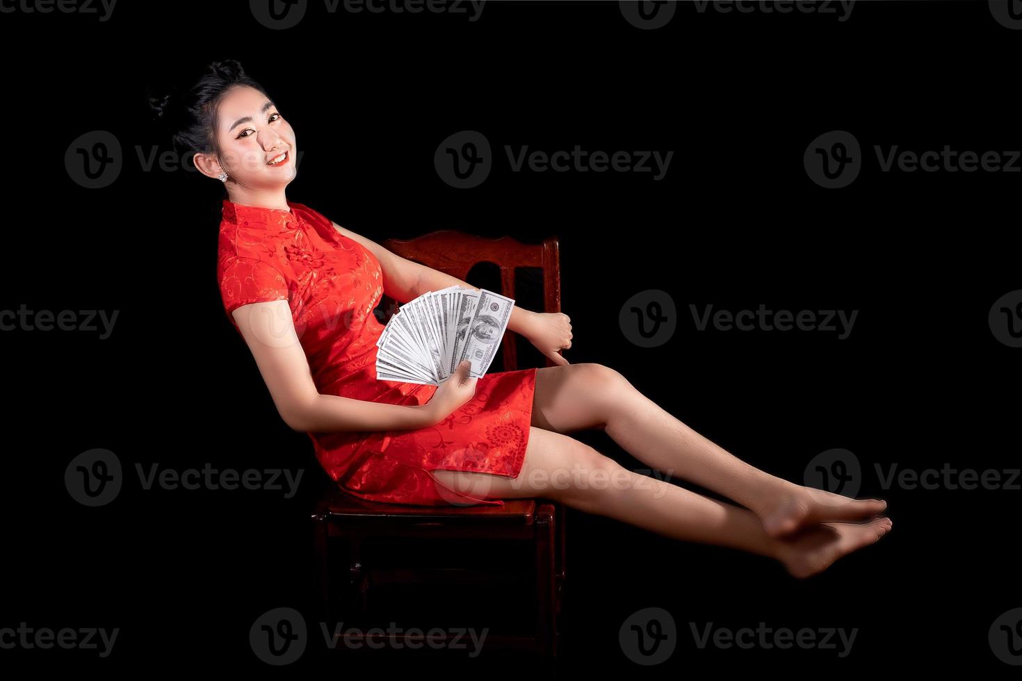 Porträt asiatische Frau rotes Kleid traditionelles Cheongsam hält Geld 100-US-Dollar-Scheine auf schwarzem Hintergrund foto