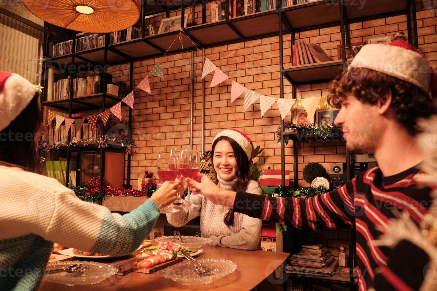 Glück Familie und Freunde feiern, heben Gläser und ein fröhliches Lächeln mit Getränken, genießen das Essen im Esszimmer des Hauses, dekoriert für Weihnachtsfest und Neujahr. foto