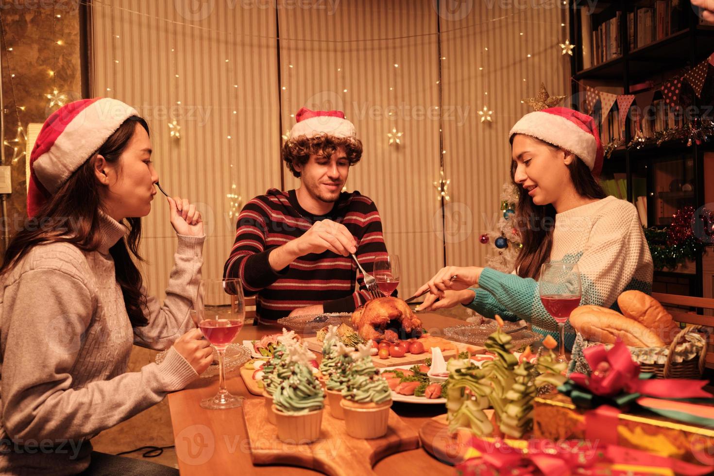 Freunde genießen es, am Tisch mit Spezialitäten zu essen, junge Frau, die im Speisesaal des Hauses gebratenen Truthahn schneidet, mit Ornamenten dekoriert, Weihnachtsfest und Neujahrsfeier. foto