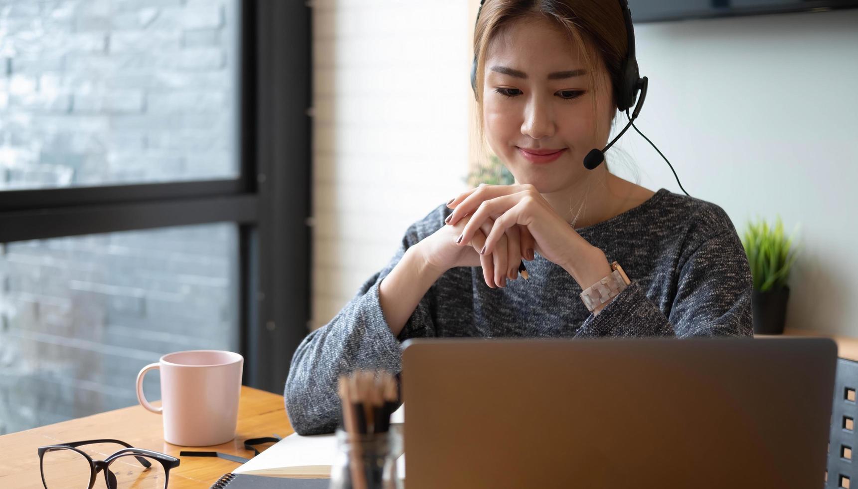 Nahaufnahme der asiatischen Frau, die online von zu Hause aus studiert und Notizen für das Fernstudium der Schüler auf dem Laptop macht, Hausaufgaben macht, Videounterricht ansieht. Fernbildungskonzept. foto