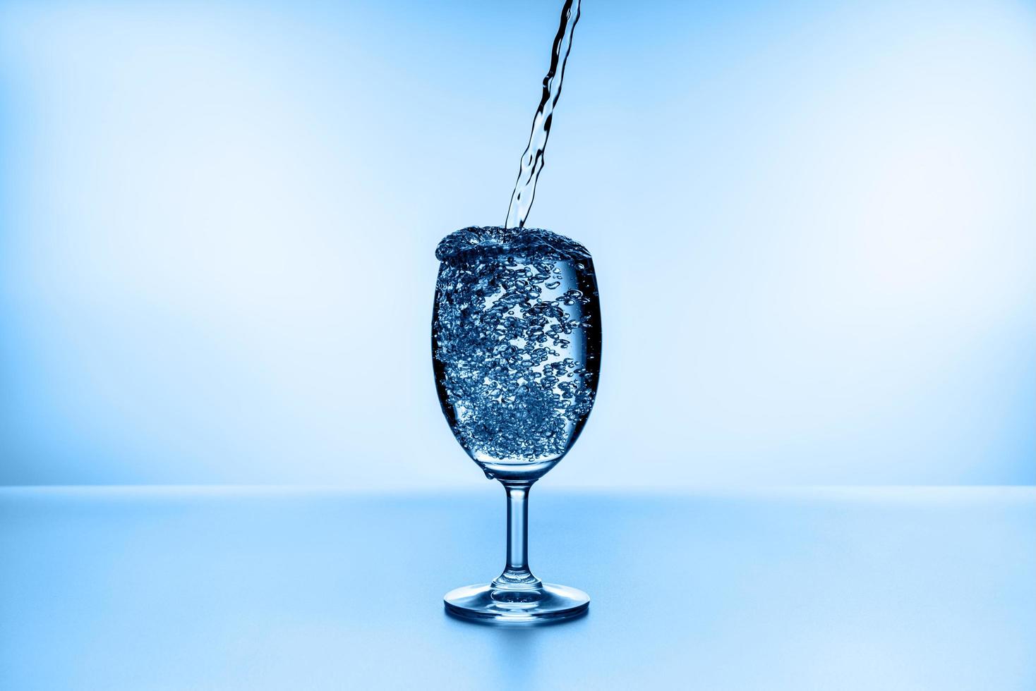 Wasser in Glas auf blauem Hintergrund gießen foto