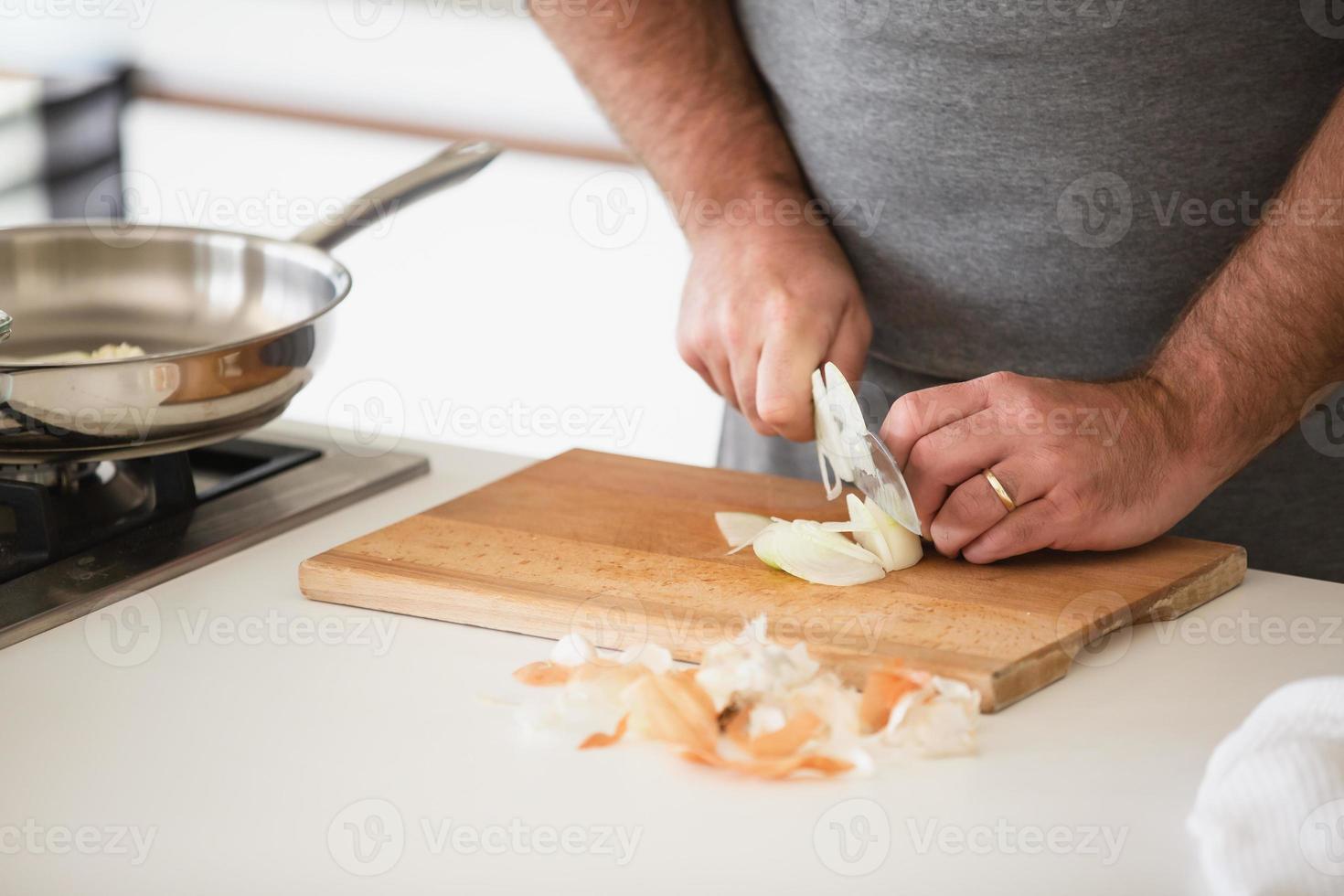 Nahaufnahme des Mannes, der Zwiebel auf Holzbrett schneidet? foto