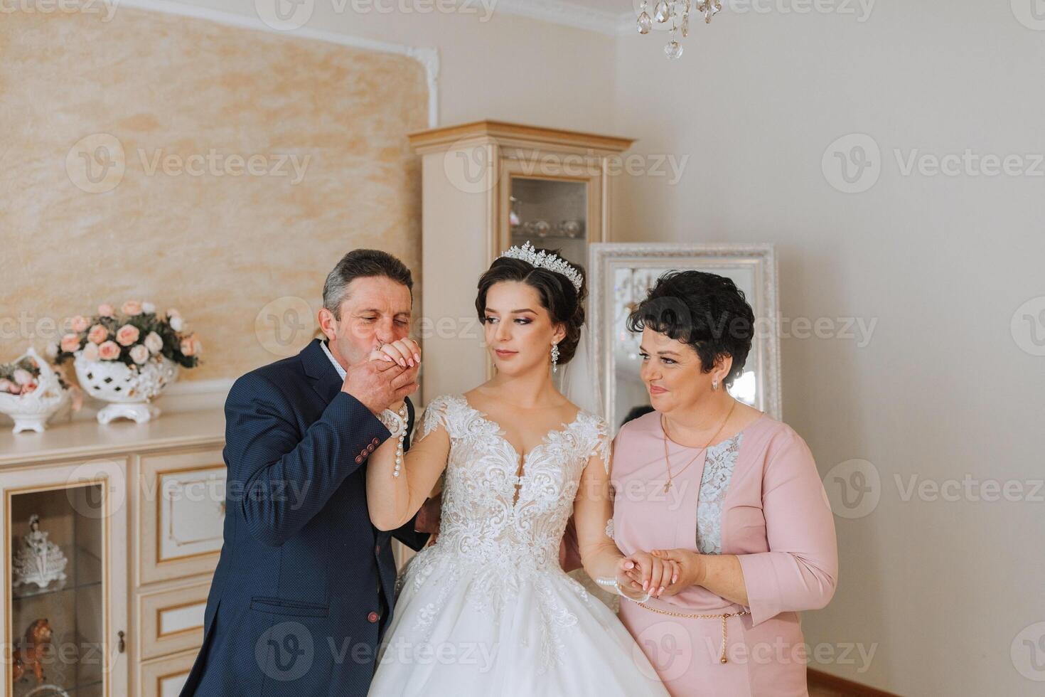 glücklich Eltern halt das Hände von das Braut Wer ist bekommen verheiratet und Unterstützung ihr, tragen ein Hochzeit Kleid und ein lange Schleier. foto