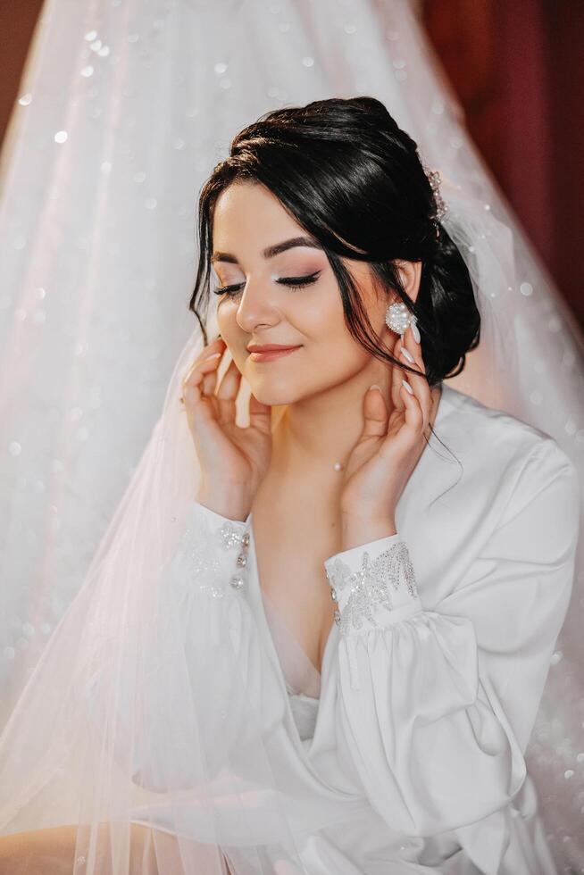 ein schön Brünette Braut mit ein Tiara im ihr Haar ist bekommen bereit zum das Hochzeit im ein schön Kleid im Boudoir Stil. Nahansicht Hochzeit Porträt, Foto. foto