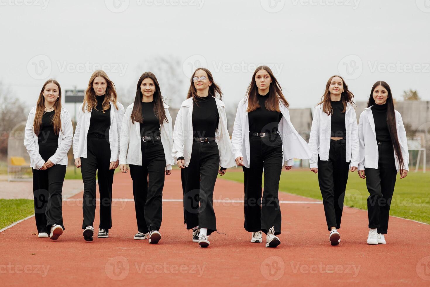 ein Gruppe von viele glücklich Teenager Mädchen gekleidet im das gleich Outfit haben Spaß und posieren im ein Stadion in der Nähe von ein Hochschule. Konzept von Freundschaft, Momente von Glück. Schule Freundschaft foto