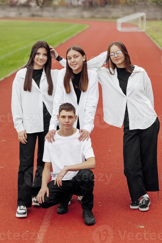 Porträt von vier Teenager im beiläufig Kleider Sitzung im ein Stadion und posieren suchen beim das Kamera. Konzept von Freundschaft. ein Moment von Glück. foto