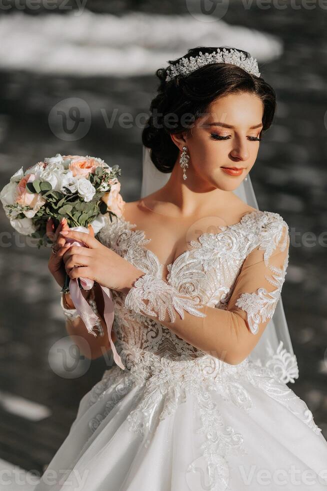 Porträt von ein schön Braut mit ein Hochzeit Strauß von Blumen, attraktiv Frau im ein Hochzeit Kleid mit ein lange Schleier. glücklich Braut Frau. Braut mit Hochzeit bilden und Frisur. Winter Hochzeit foto