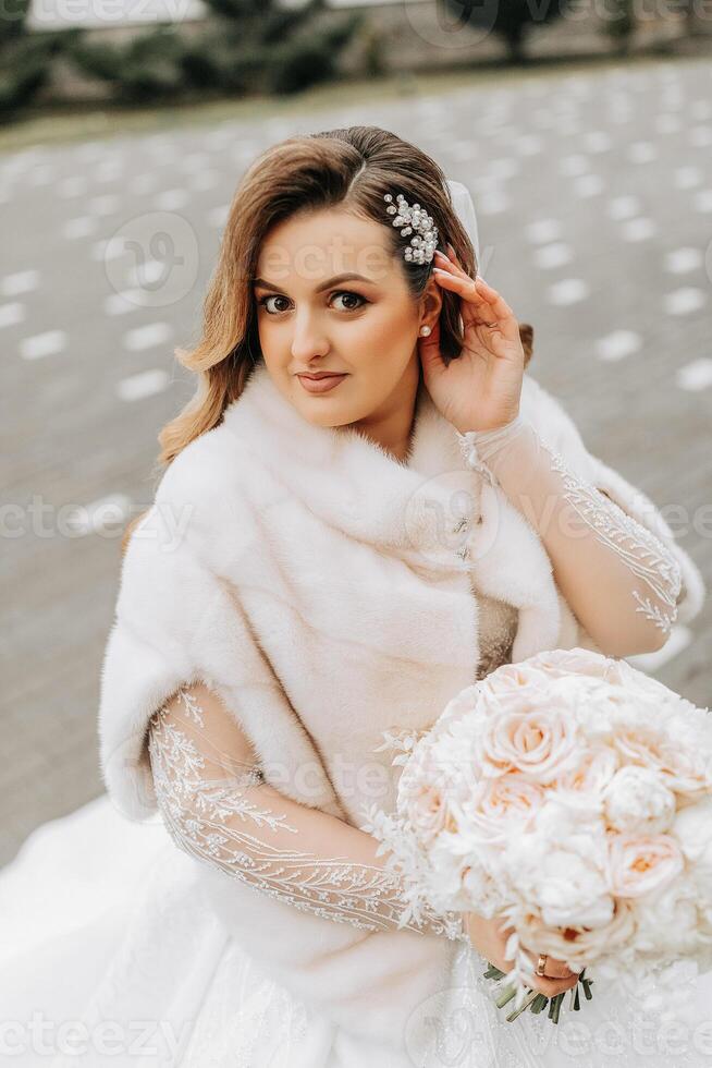 Porträt von ein schön Braut mit ein Hochzeit Strauß von Blumen, attraktiv Frau im ein Hochzeit Kleid mit ein lange Schleier. glücklich Braut Frau. Braut mit Hochzeit bilden und Frisur. Winter Hochzeit foto