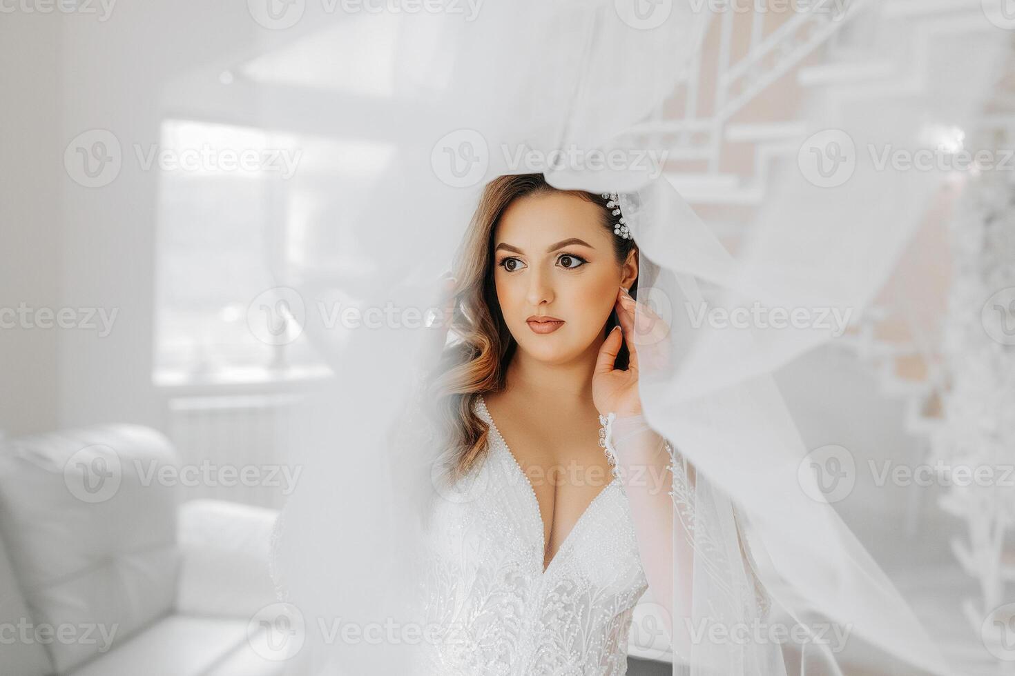 Porträt von ein zärtlich Braut im ein Hochzeit Kleid und ein schön Frisur unter ein Schleier im ihr Zimmer von das Morgen foto