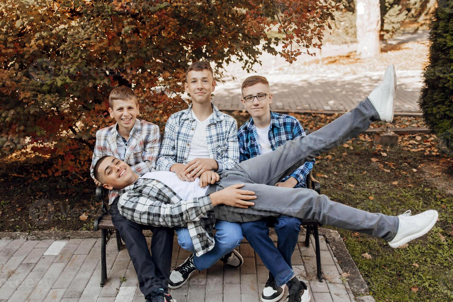 vier Jugendliche sind haben Spaß und Sein glücklich während Sitzung auf ein Park Bank. Teenager Klassenkameraden sind ruhen gegen das Hintergrund von Herbst Natur. foto