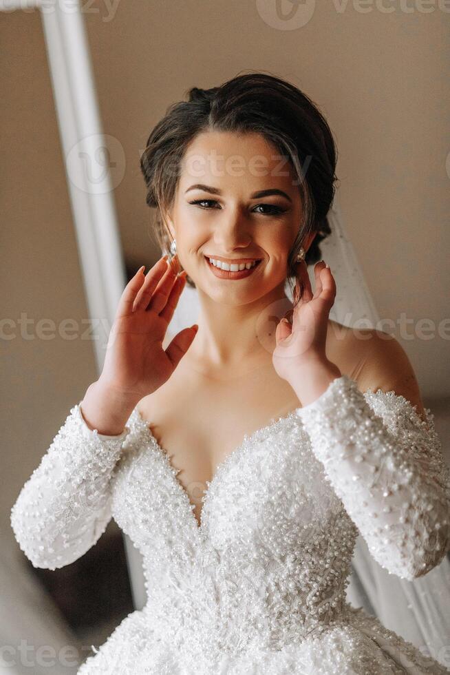 ein Braut im ein Hochzeit Kleid mit lange Ärmel posiert im ihr Zimmer. Morgen von das Braut. Vorbereitung. Hochzeit Fotografie foto