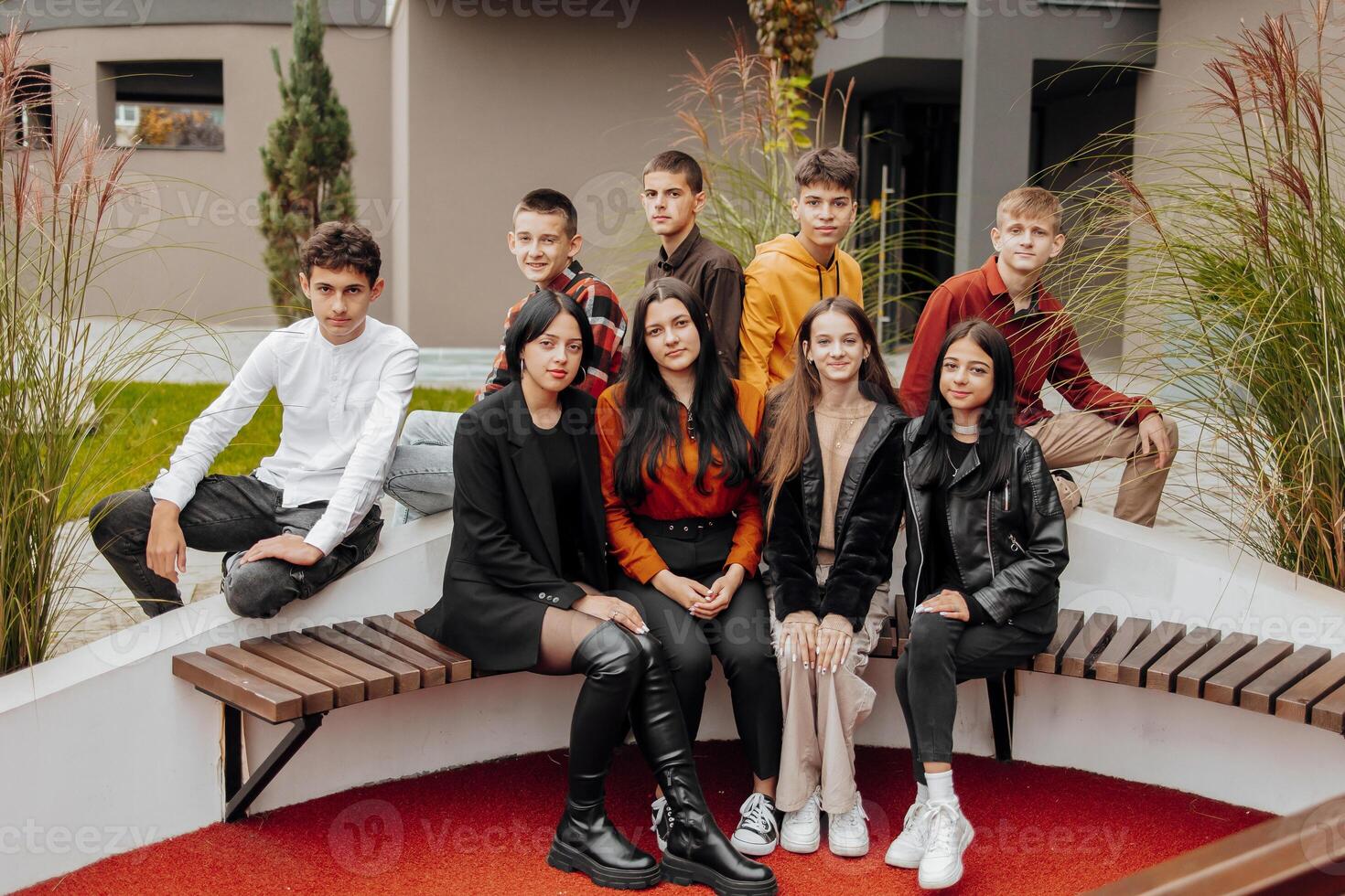 Gruppe von lächelnd und glücklich Teenager freunde tragen beiläufig Kleider Ausgaben Zeit zusammen, posieren und reden mit jeder andere in der Nähe von Hochschule Gebäude auf Herbst Tag. foto