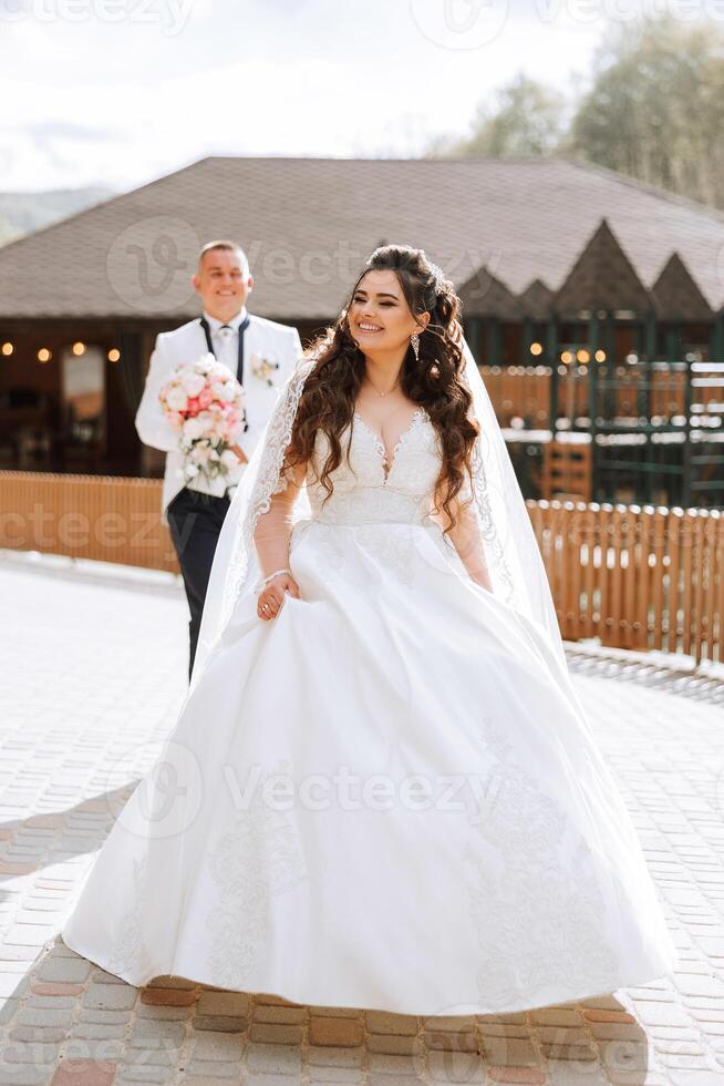 ein schön jung Braut, im ein Sommer- Park, Spaziergänge voraus von ihr Bräutigam. schön Hochzeit Weiß Kleid. Spaziergänge im das Park. ein glücklich und liebend Paar. foto