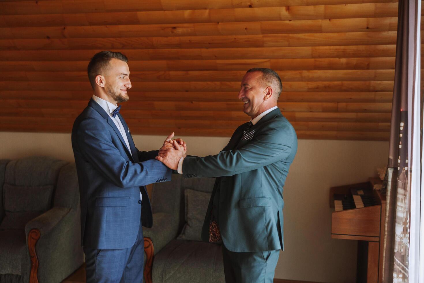 ein Vater Umarmungen seine reifen Sohn und hilft ihm bereiten zum das Hochzeit Zeremonie. warm und aufrichtig Beziehungen zwischen ein Vater und ein Erwachsene Sohn. ein emotional Moment beim ein Hochzeit foto