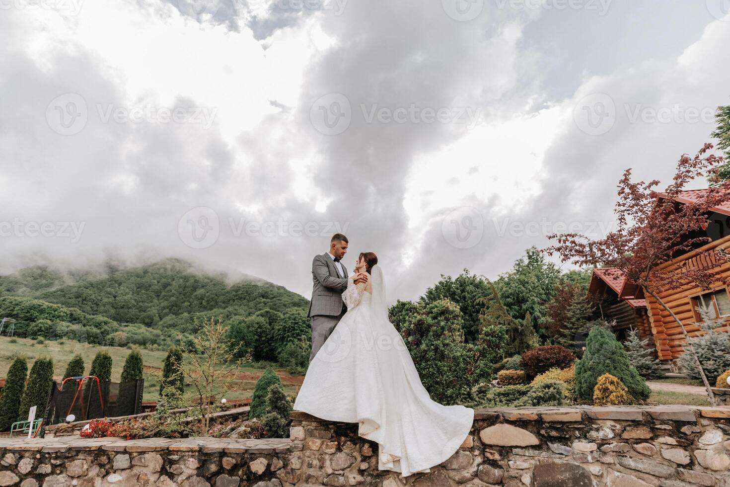 Hochzeit. Liebe und Paar im Garten zum Hochzeit. Feier von Zeremonie und Engagement. speichern das Datum. Vertrauen. das Bräutigam umarmt das Braut gegen das Hintergrund von Berge und ein wolkig Himmel. foto