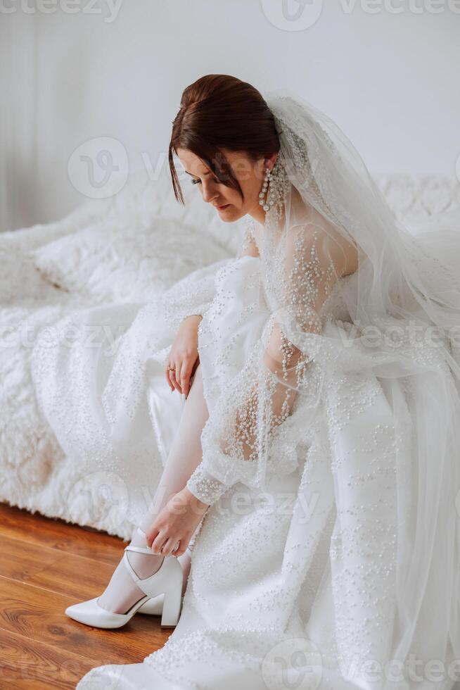 jung Braut im schön Hochzeit Kleid Putten auf Schuhe drinnen, Nahansicht. das Braut im ein Hochzeit Kleid und ein schön Frisur. foto