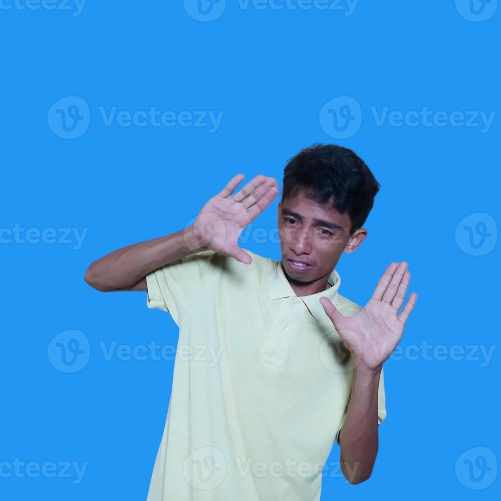 jung asiatisch Mann Hände stoppen. mit ein ernst Gesicht tragen ein Gelb T-Shirt, isoliert auf ein Blau Hintergrund foto