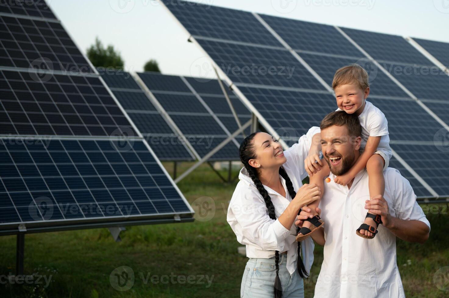 ein breit Schuss von ein glücklich Familie Stehen zusammen und lächelnd beim Kamera mit ein groß Solar- Panel im Hintergrund foto