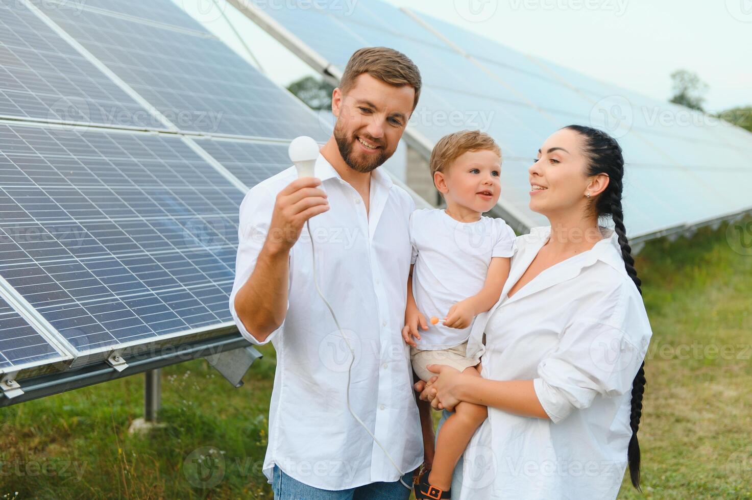 Solar- Energie Konzept. ein jung, glücklich Familie ist Stehen in der Nähe von Solar- Paneele und halten ein elektrisch Licht Birne. foto