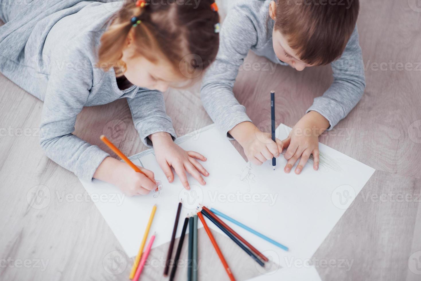 Kinder liegen im Schlafanzug auf dem Boden und zeichnen mit Bleistiften. süßes Kind malen mit Bleistiften foto