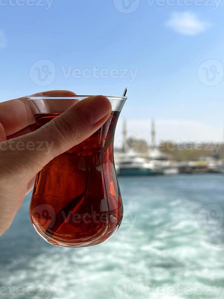 ein Tasse von Tee im ein Frau Hand gegen das Hintergrund von das Bosporus und Istanbul foto