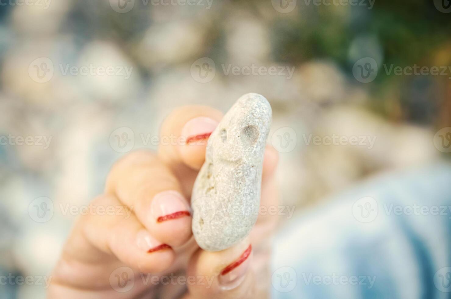 Frau mit Maniküre halten ein Meer Stein im Finger im hell Sonne Licht mit stark Bokeh foto