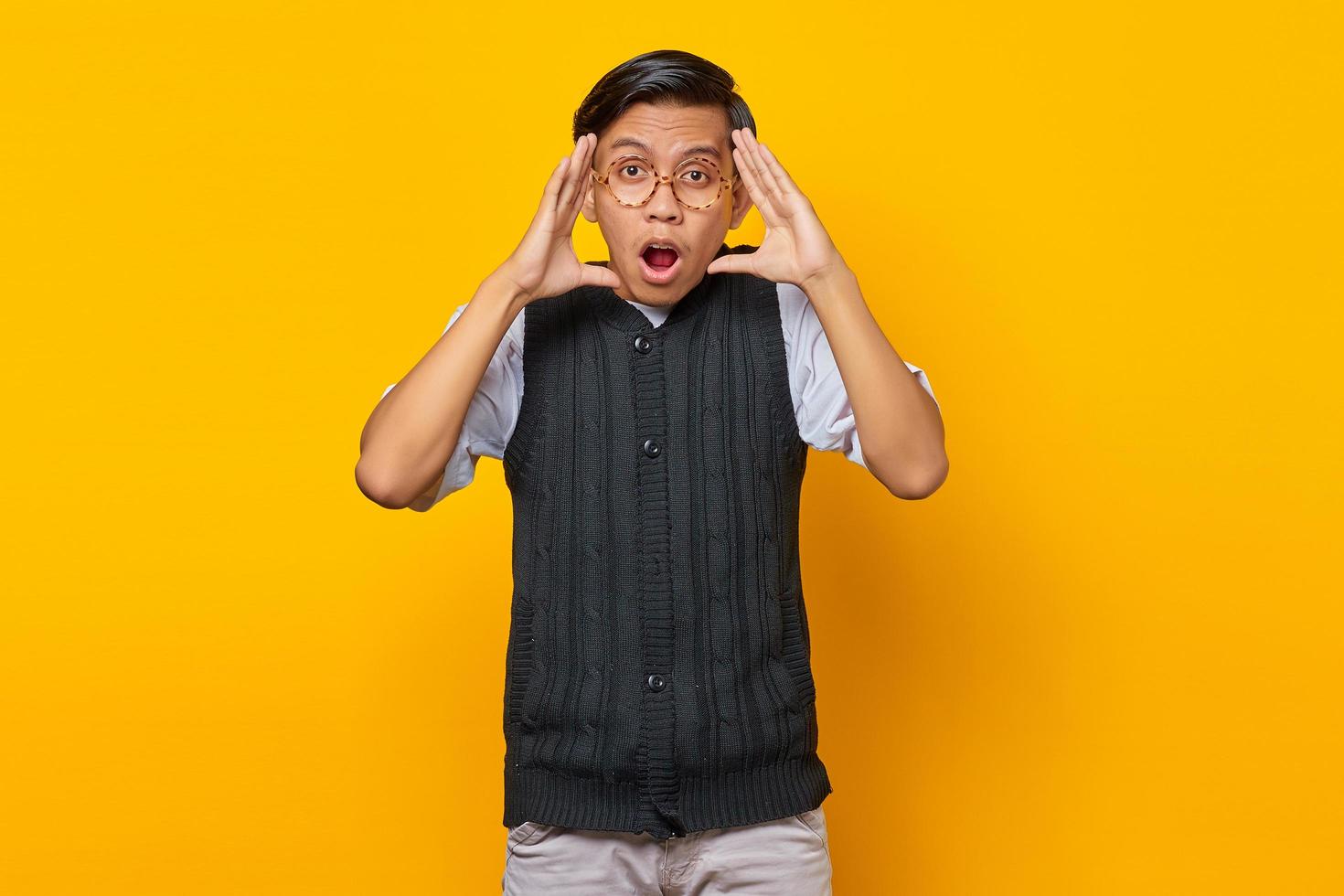 Porträt des schockierten asiatischen jungen Mannes, der Kamera auf gelbem Hintergrund schaut foto