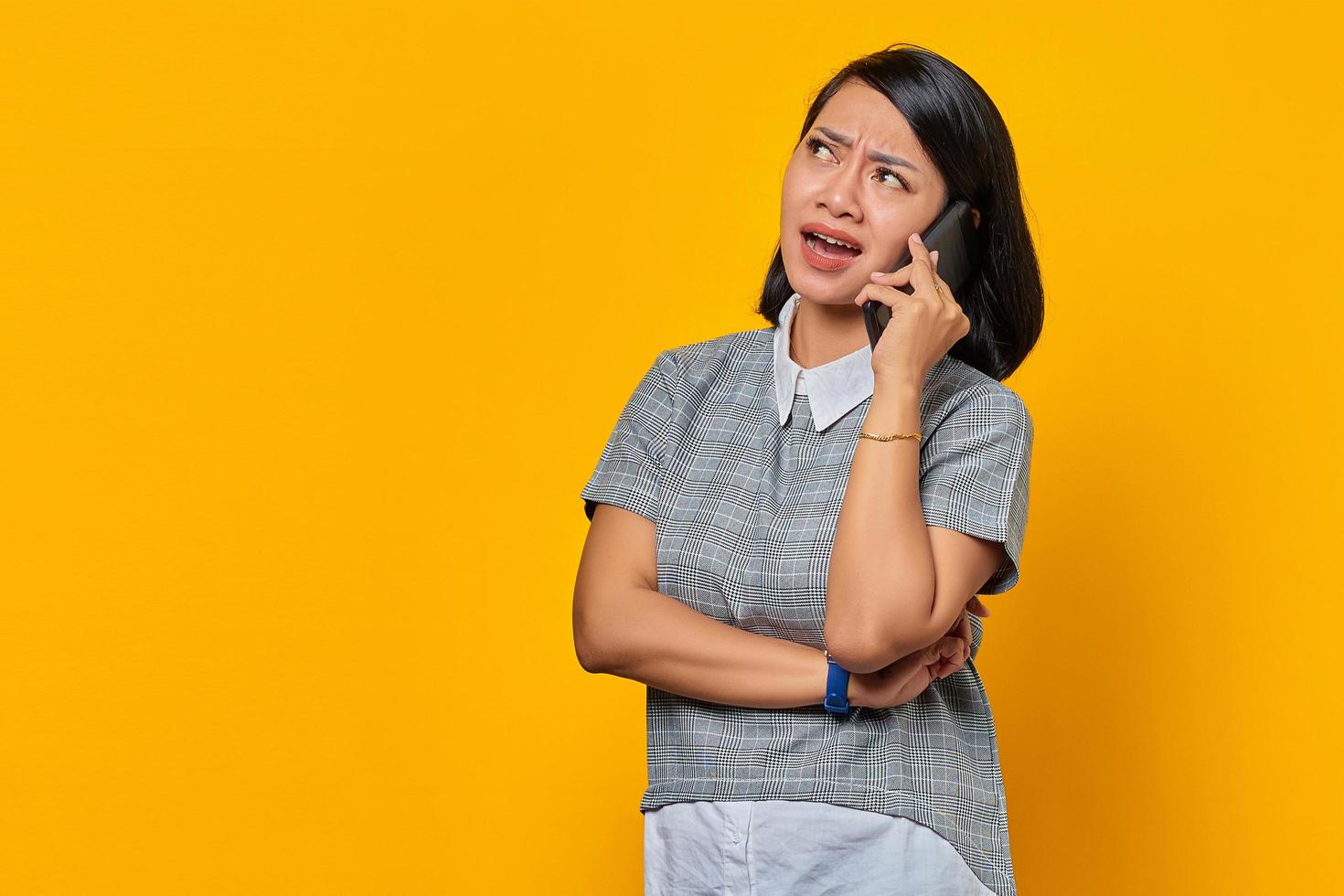 Porträt einer wütenden jungen asiatischen Frau beim Empfang eines eingehenden Anrufs auf dem Smartphone auf gelbem Hintergrund foto