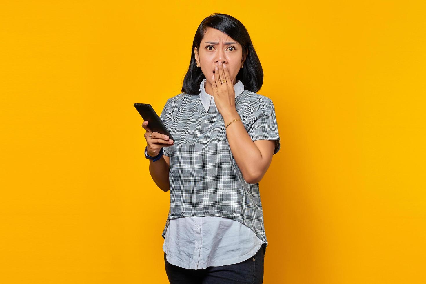 Porträt einer schockierten jungen Asiatin, die Smartphone hält und den Mund mit der Hand bedeckt foto