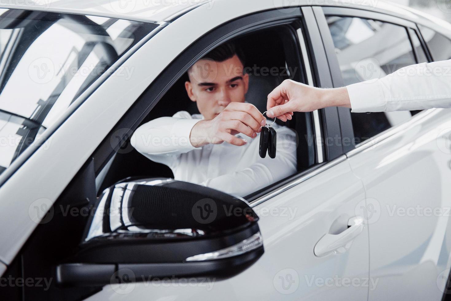 Zwei Männer stehen im Ausstellungsraum gegen Autos. Nahaufnahme eines Verkaufsleiters in einem Anzug, der einem Kunden ein Auto verkauft. der Verkäufer übergibt dem Kunden den Schlüssel. foto