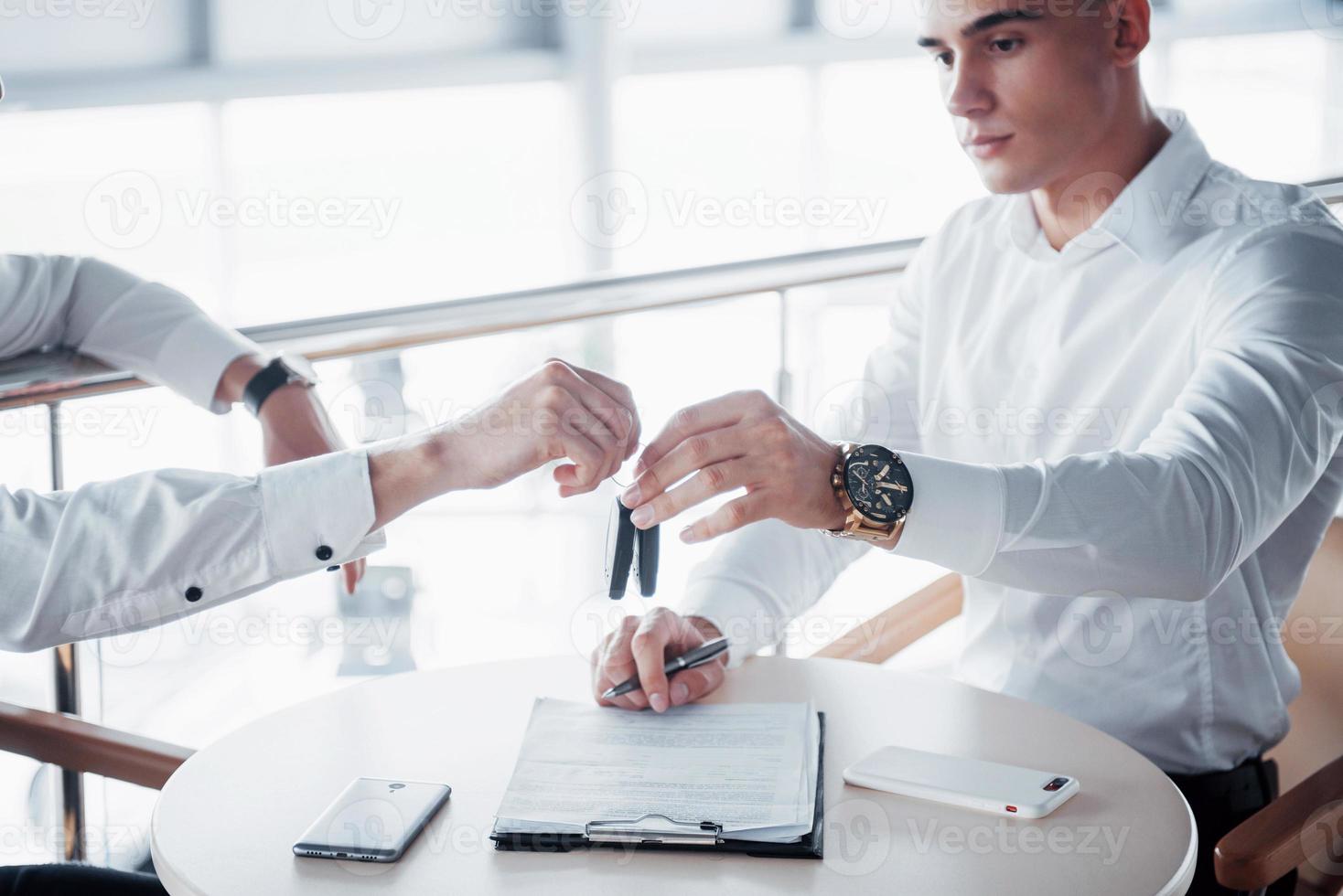 ein junger Mann unterschreibt im Büro Dokumente, erfolgreiche Verkäufe und Schlüsselübergaben an den Kunden foto