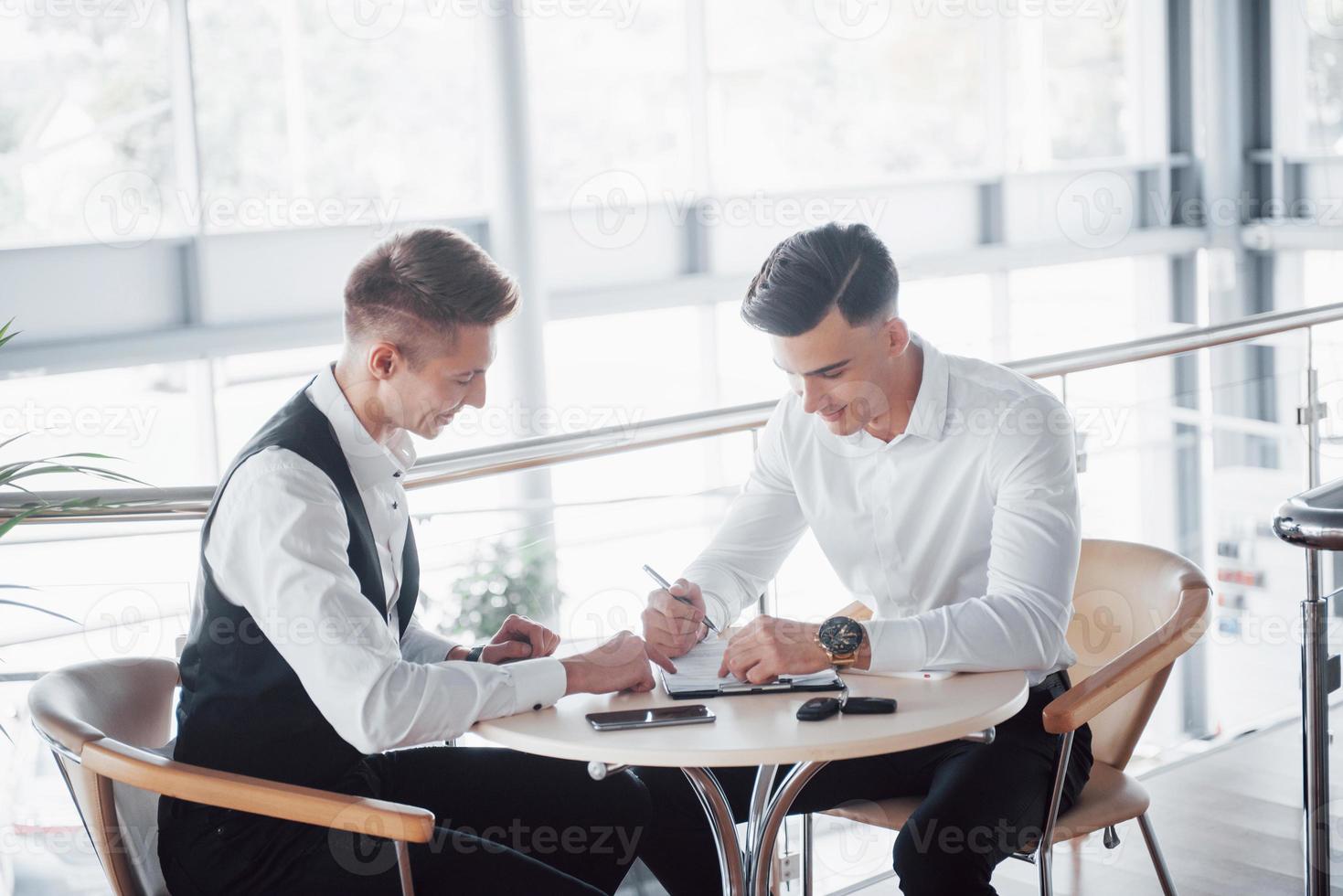 zwei Geschäftsleute unterschreiben Dokumente in einem großen, geräumigen Büro foto